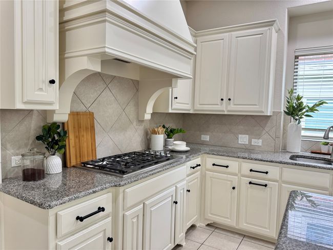 Kitchen with stainless steel gas cooktop, custom range hood, tasteful backsplash, and light tile patterned floors | Image 4