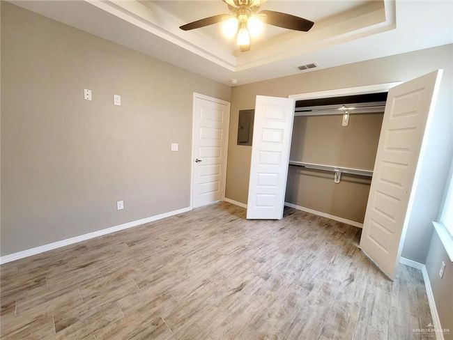 Unfurnished bedroom featuring a tray ceiling, electric panel, wood finished floors, and a closet | Image 15