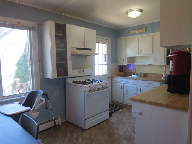 Kitchen with under cabinet range hood, a sink, gas range gas stove, black microwave, and baseboard heating | Image 19