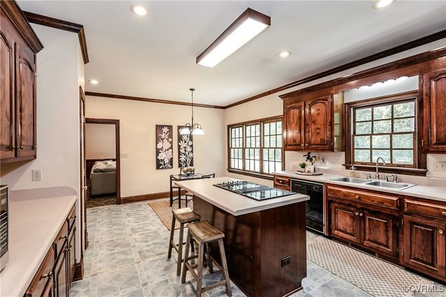 Kitchen with black appliances, a sink, a center island, light countertops, and ornamental molding | Image 27