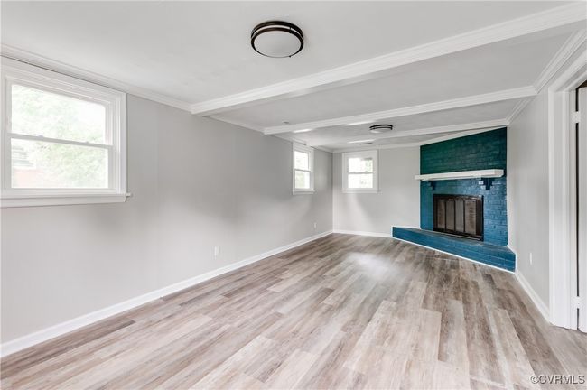 Unfurnished living room with a fireplace, crown molding, light wood-style floors, and beamed ceiling | Image 17