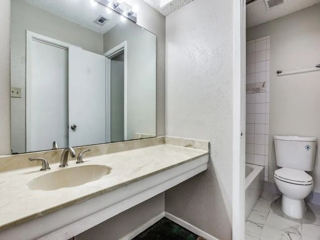 Bathroom featuring vanity, bathtub / shower combination, a textured wall, and marble finish flooring | Image 10