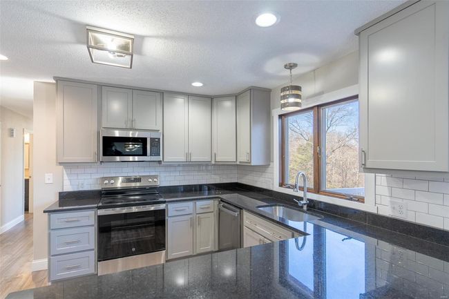 Kitchen featuring gray cabinetry, sink, pendant lighting, and appliances with stainless steel finishes | Image 39