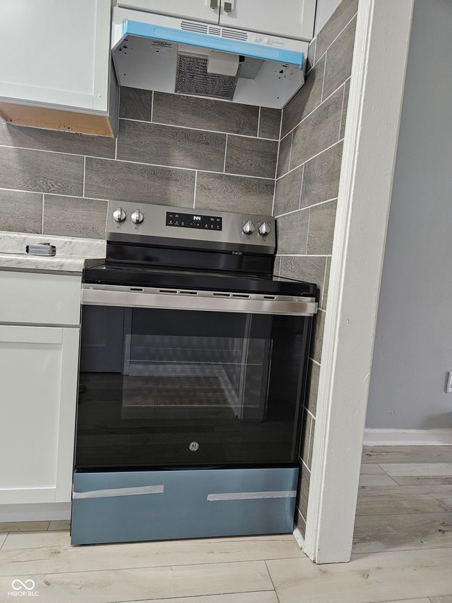 kitchen view of stainless steel electric range oven, under cabinet range hood, white cabinetry, and light wood-style flooring | Image 13