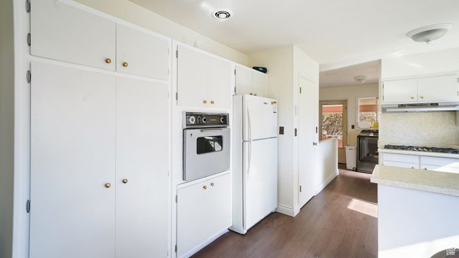 Kitchen with white appliances, under cabinet range hood, dark wood finished floors, light countertops, and white cabinetry | Image 6