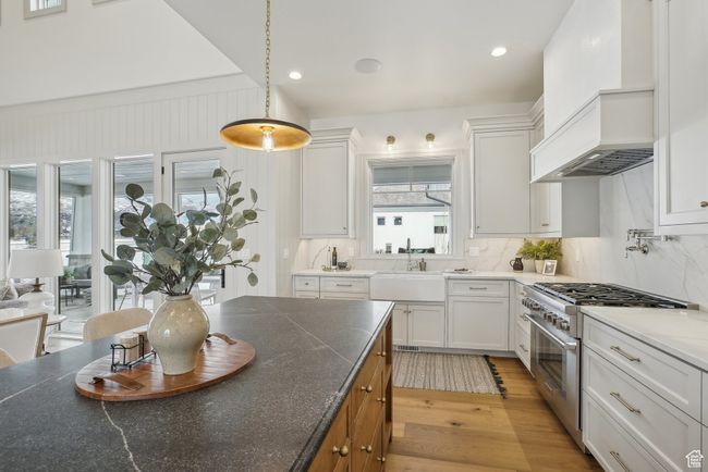 Kitchen with decorative light fixtures, light wood-style flooring, white cabinetry, a sink, and high end stove | Image 15