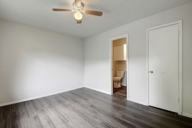 Unfurnished bedroom featuring wood finished floors, ensuite bathroom, baseboards, a textured ceiling, and ceiling fan | Image 15