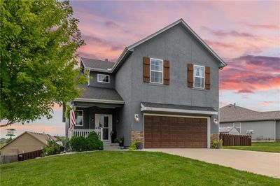 View of property featuring a garage, a porch, and a lawn | Image 1