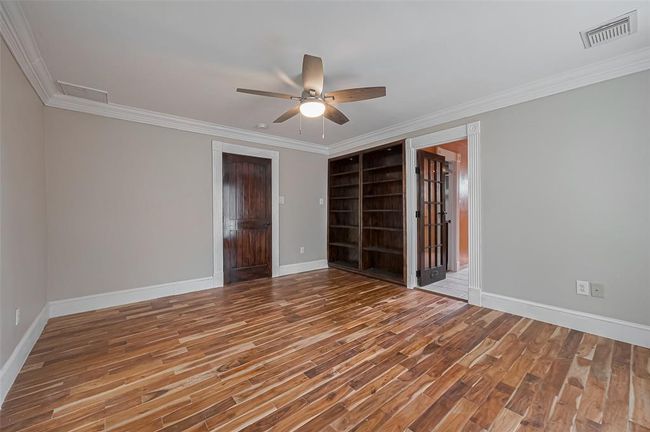 This upstairs primary retreat boasts hardwood-style flooring, built-in bookcases, and French doors into the en-suite bath. Accented with crown molding and extended baseboards. | Image 31