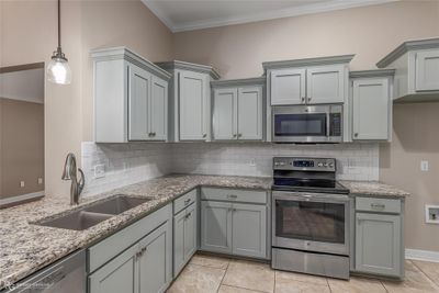 Kitchen featuring decorative backsplash, light stone counters, stainless steel appliances, crown molding, and sink | Image 3