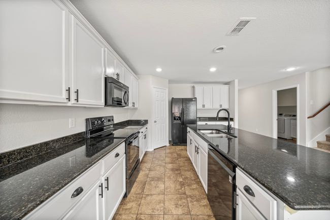 Kitchen featuring black appliances, washing machine and clothes dryer, white cabinets, recessed lighting, and a center island with sink | Image 15