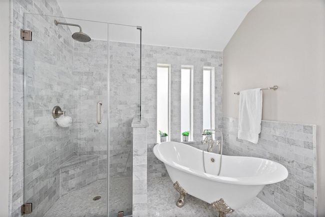 Custom clawfoot tub with vintage-inspired faucet, marble mosaic floors, marble subway tile, seamless glass shower, and marble-topped vanities. | Image 27