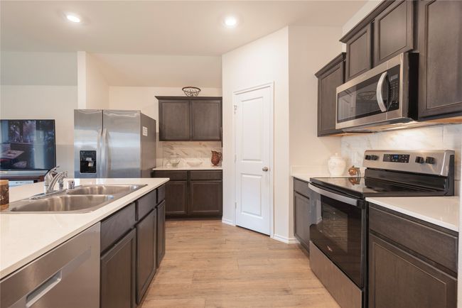 Kitchen featuring stainless steel appliances, light wood-style flooring, tasteful backsplash, dark brown cabinets, and light countertops | Image 22