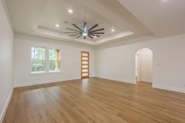 Step into a bright and expansive open-concept living area featuring rich wood-style flooring, recessed lighting, and an eye-catching statement ceiling fan. The layout effortlessly flows into the kitchen, creating an ideal space for both relaxing and entertaining. | Image 4