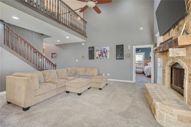 Living room with a towering ceiling, a fireplace, carpet floors, ceiling fan, and stairway | Image 6