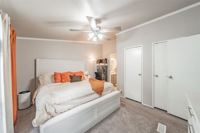 Bedroom with crown molding, light colored carpet, multiple closets, a ceiling fan, and ensuite bath | Image 18