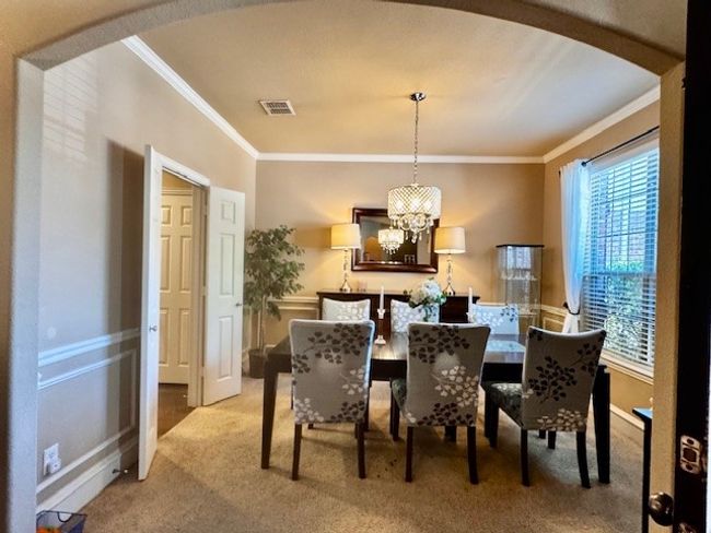 Dining area featuring a chandelier, light carpet, ornamental molding, and visible vents | Image 6