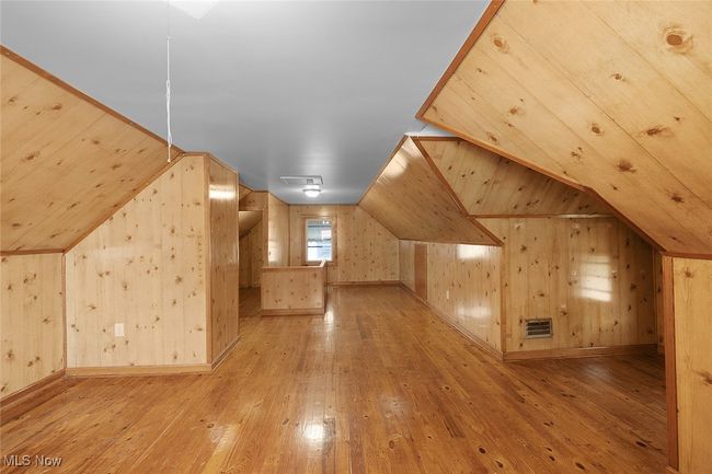 Primary bedroom with lofted ceiling, wooden walls, hardwood / wood-style floors, and visible vents | Image 19