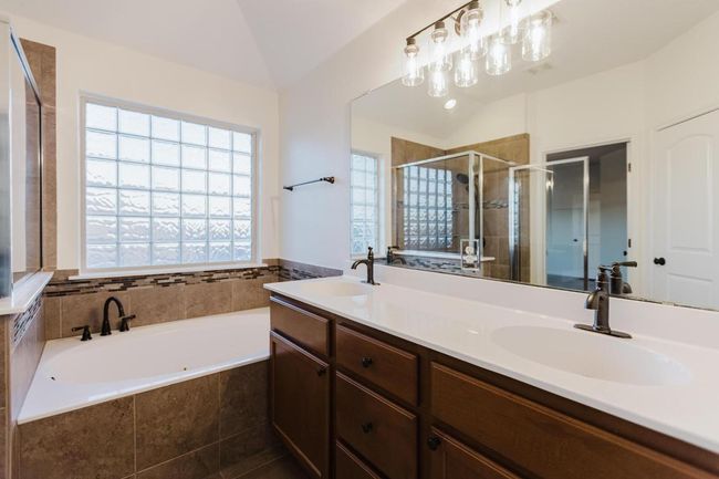 Bathroom featuring double vanity, a stall shower, a sink, vaulted ceiling, and a garden tub | Image 31