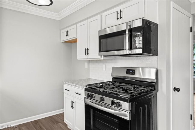Kitchen with decorative backsplash, dark wood-type flooring, crown molding, white cabinets, and appliances with stainless steel finishes | Image 19