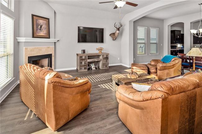 Living room with ceiling fan with notable chandelier, plenty of natural light, dark wood-type flooring, and a tiled fireplace | Image 12