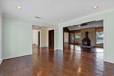 Unfurnished living room featuring a wood stove, ornamental molding, brick wall, and dark wood-type flooring | Image 3