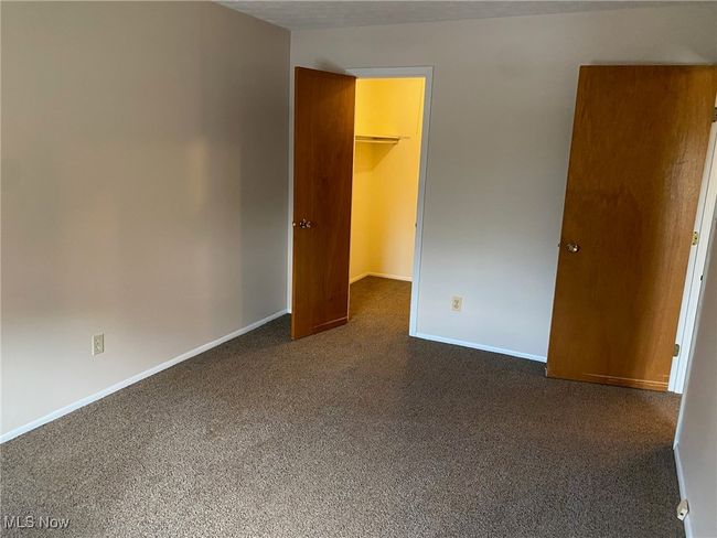 Unfurnished bedroom with a walk in closet, baseboards, dark carpet, and a closet | Image 11