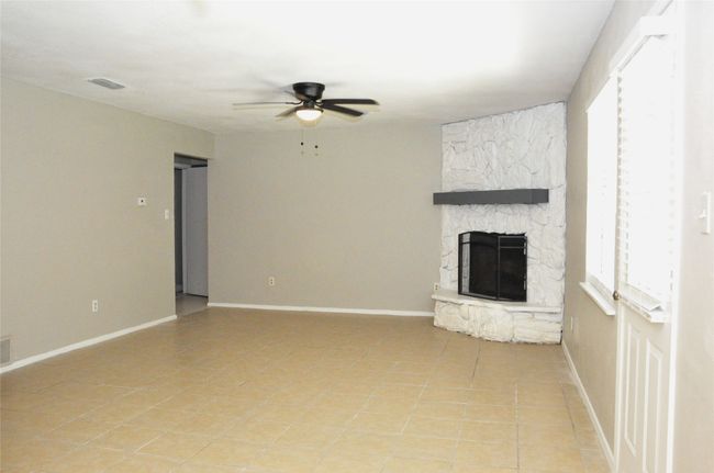 Unfurnished living room featuring a ceiling fan, visible vents, baseboards, and a fireplace | Image 6