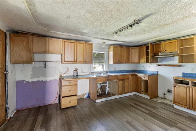Kitchen featuring under cabinet range hood, dark wood-style floors, open shelves, a textured ceiling, and brown cabinets | Image 10