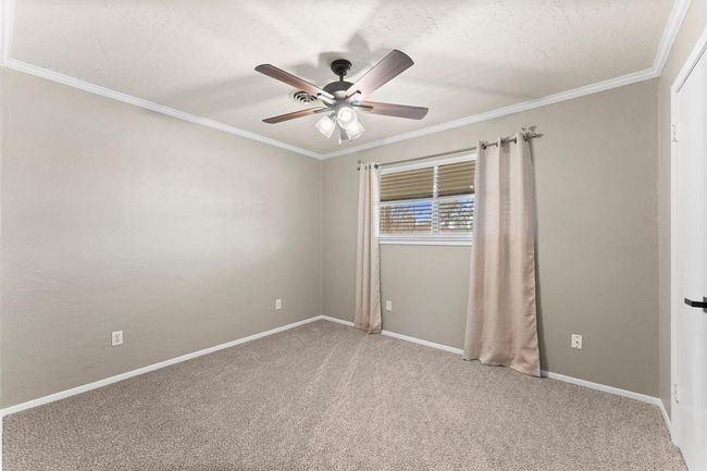 This bedroom features neutral walls and carpet, a ceiling fan with lights, and a window with curtains, providing a cozy space with plenty of natural light. | Image 22