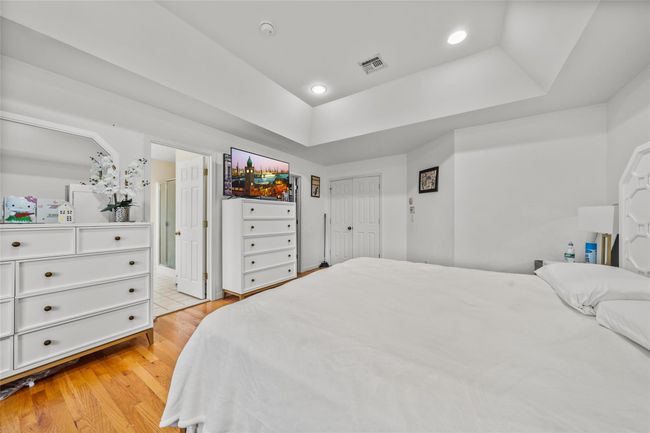 Bedroom with visible vents, light wood-style floors, a tray ceiling, recessed lighting, and ensuite bath | Image 23