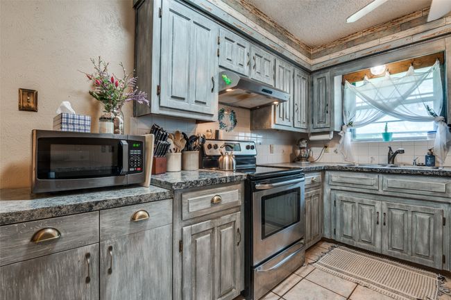 Kitchen with a textured ceiling, under cabinet range hood, a sink, appliances with stainless steel finishes, and backsplash | Image 11