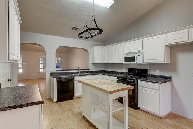 Kitchen featuring black appliances, wooden counters, arched walkways, white cabinetry, and lofted ceiling | Image 11