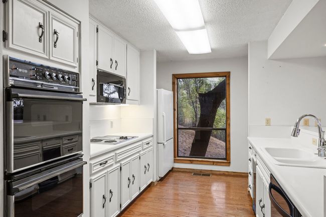 Kitchen with black appliances, a textured ceiling, white cabinetry, light countertops, and light wood finished floors | Image 21