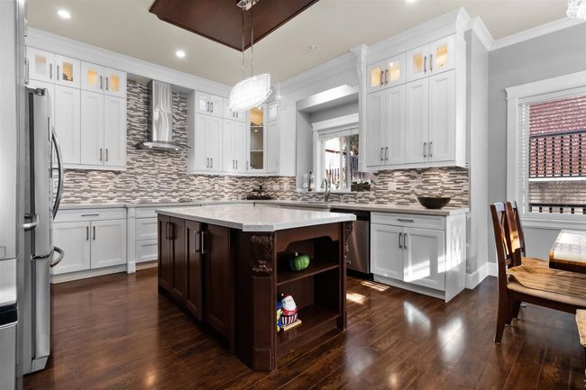 Kitchen featuring wall chimney exhaust hood, stainless steel appliances, ornamental molding, tasteful backsplash, and a kitchen island | Image 11