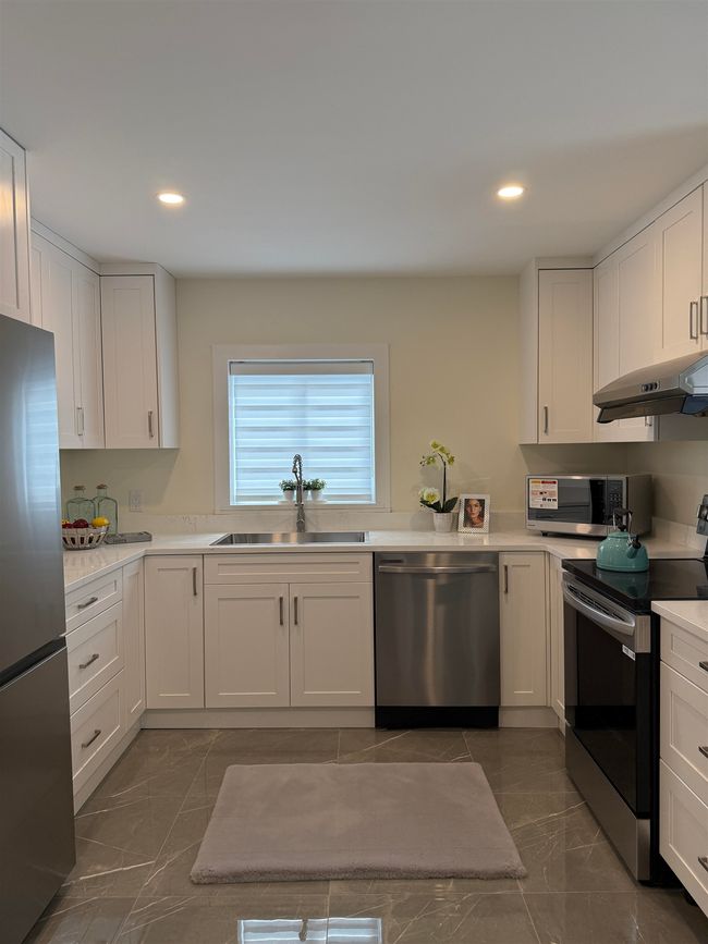 Kitchen with appliances with stainless steel finishes, under cabinet range hood, white cabinets, dark marble finish floors, and light countertops | Image 7