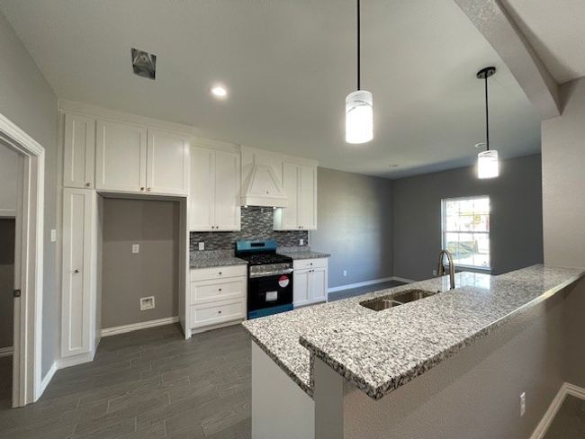 Kitchen with granite countertop, backsplash, stainless steel range with gas cooktop, white cabinets, and a sink | Image 7