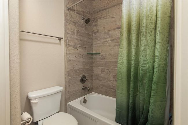 This bathroom features a modern tub and shower with a sleek tile surround, and a standard toilet, offering a clean and functional space. | Image 38