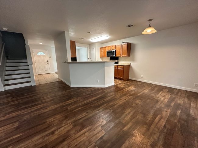 Kitchen with brown cabinets, dark wood finished floors, a peninsula, stainless steel microwave, and pendant lighting | Image 10