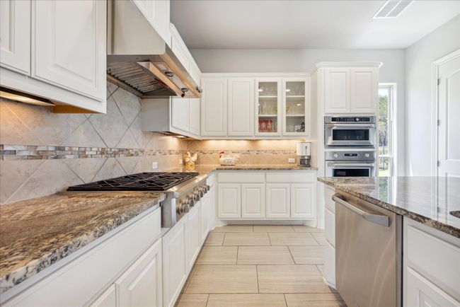 Kitchen featuring backsplash, under cabinet range hood, stainless steel appliances, visible vents, and white cabinets | Image 11