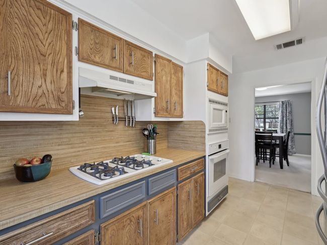 Kitchen with white appliances, light countertops, backsplash, under cabinet range hood, and visible vents | Image 12