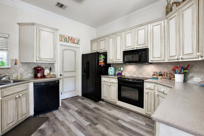 Kitchen featuring black appliances, cream cabinetry, backsplash, light wood-style floors, and ornamental molding | Image 11