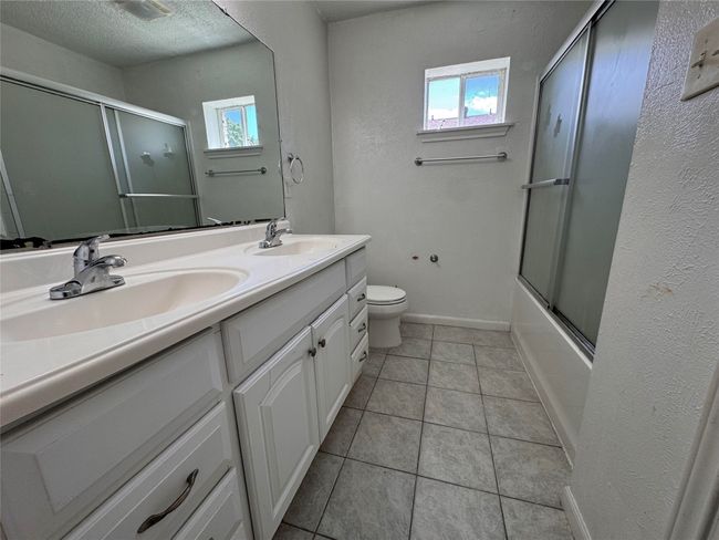 Bathroom with double vanity, tile patterned floors, a textured ceiling, and enclosed tub / shower combo | Image 7