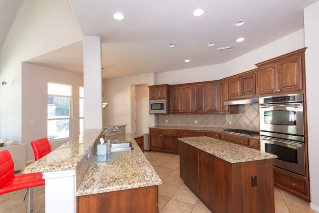 Kitchen with tasteful backsplash, a sink, appliances with stainless steel finishes, under cabinet range hood, and a kitchen island | Image 5