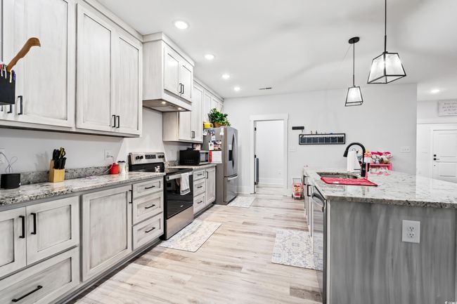 Kitchen featuring appliances with stainless steel finishes, a center island with sink, recessed lighting, light wood-style floors, and pendant lighting | Image 7