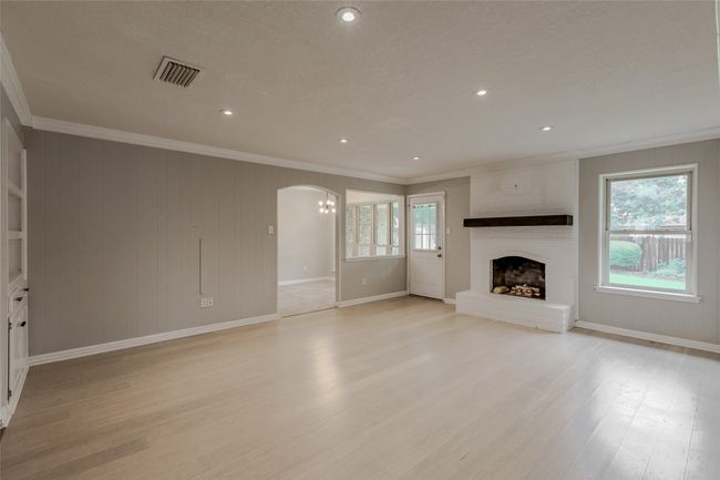 Unfurnished living room with crown molding, light wood-style flooring, arched walkways, a fireplace, and recessed lighting | Image 5