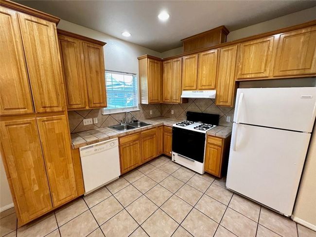 Kitchen with white appliances, tile counters, under cabinet range hood, backsplash, and recessed lighting | Image 5