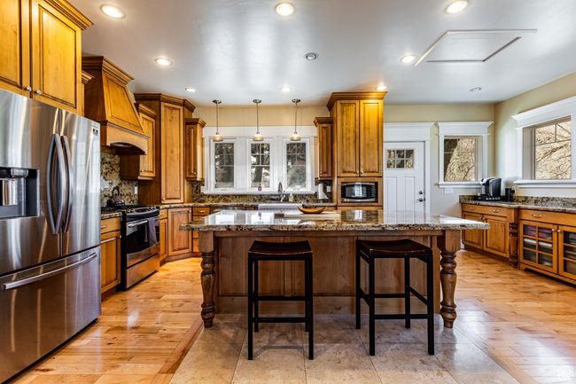 Kitchen featuring stainless steel appliances, a breakfast bar, a sink, a kitchen island, and brown cabinets | Image 8