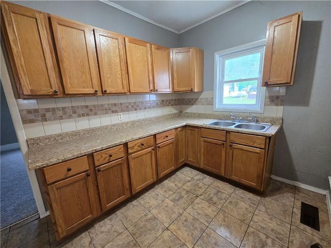 Kitchen with a sink, tasteful backsplash, light countertops, crown molding, and brown cabinets | Image 8