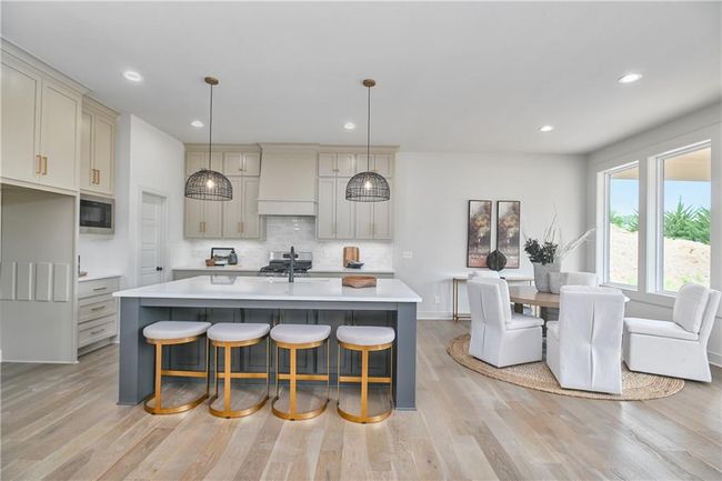 Kitchen with stainless steel microwave, light hardwood / wood-style flooring, custom exhaust hood, decorative backsplash, and a center island with sink | Image 11
